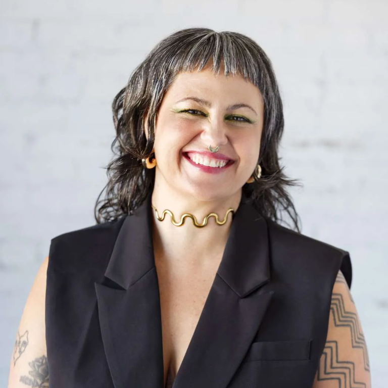 Person smiling in black vest with tattoos.