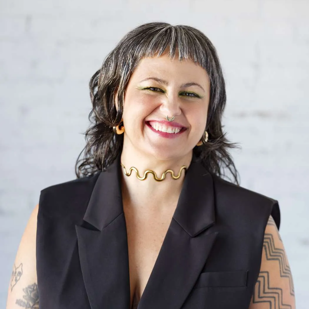 Person smiling in black vest with tattoos.