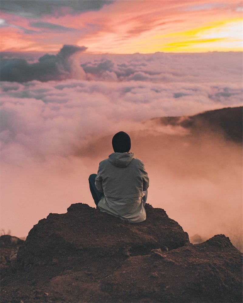 Person sitting above clouds at sunset.